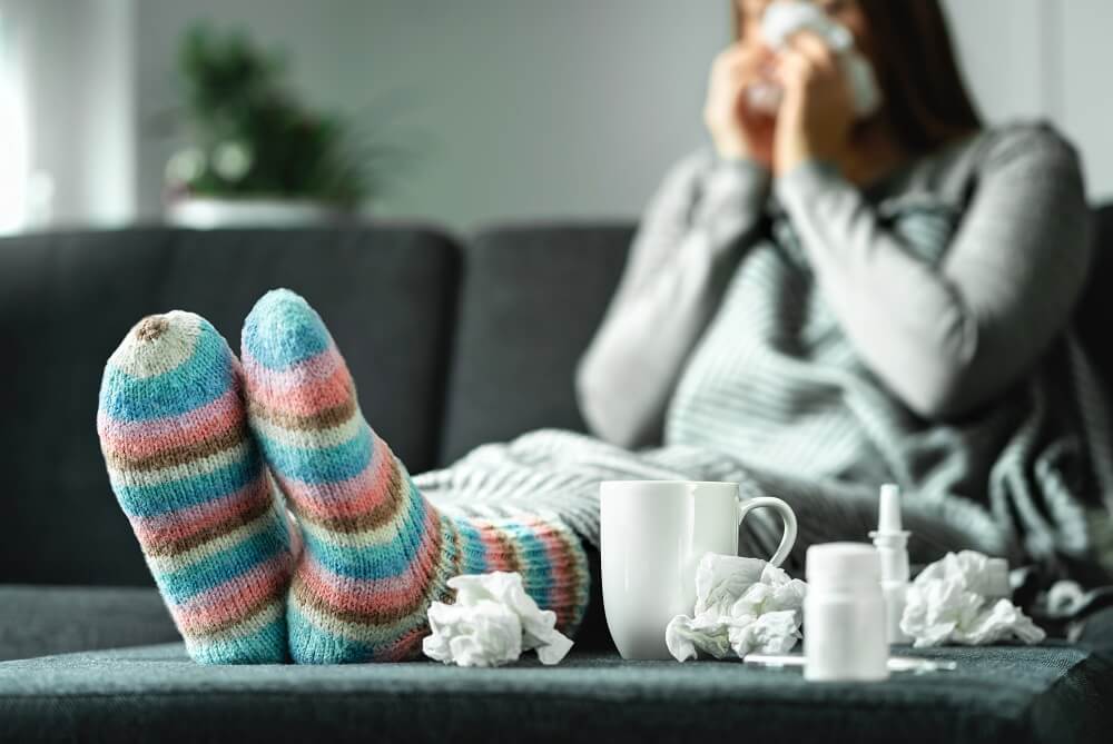Frau mit Erkältung sitzt auf Sofa und putzt sich die Nase