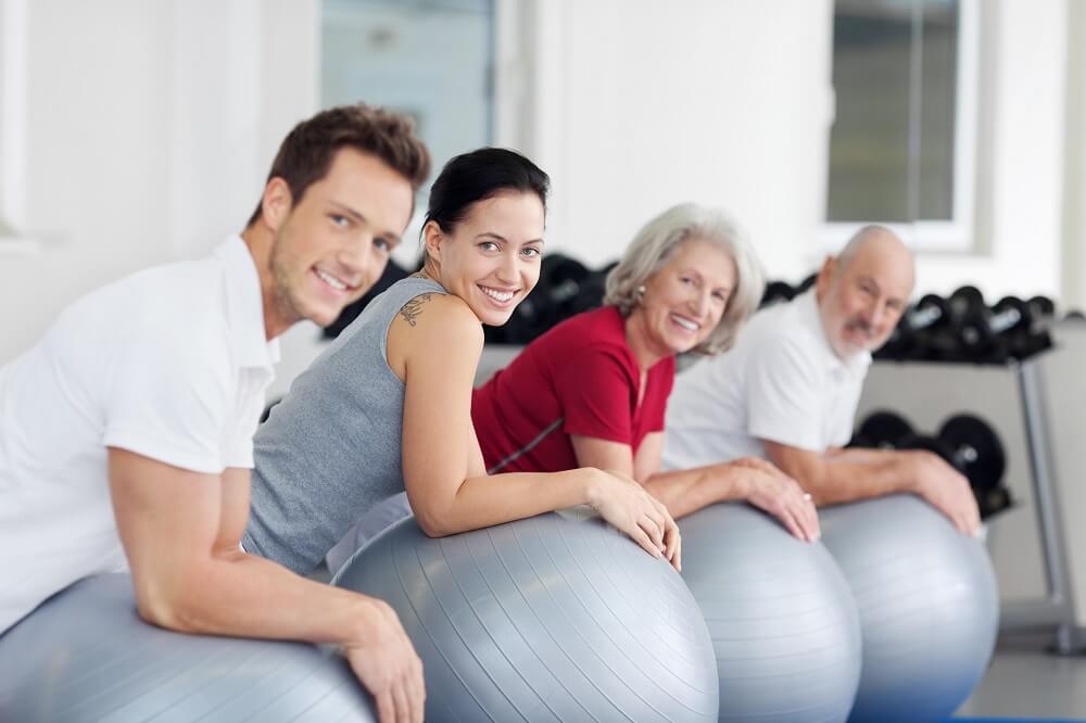 Gruppe von Menschen auf großen Gymnastikbällen bei Rückengymnastik