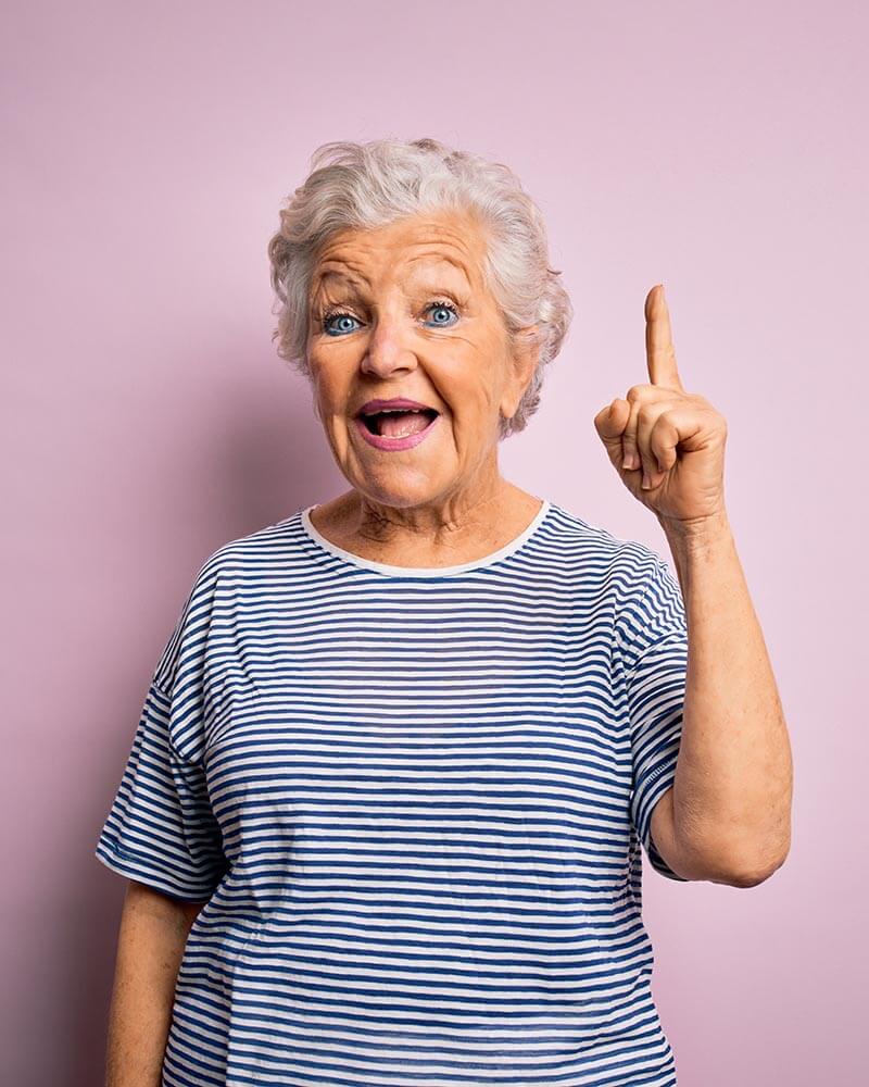 Seniorin vor lila Hintergrund zeigt lachend nach oben