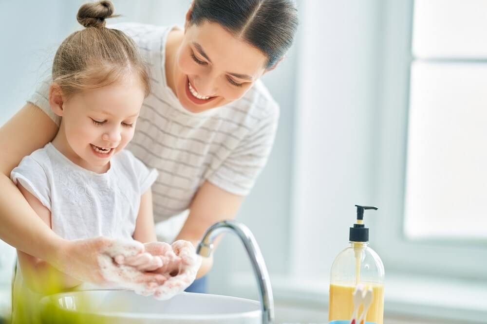 Junge Mutter wäscht mit kleiner Tochter zusammen die Hände im Waschbecken