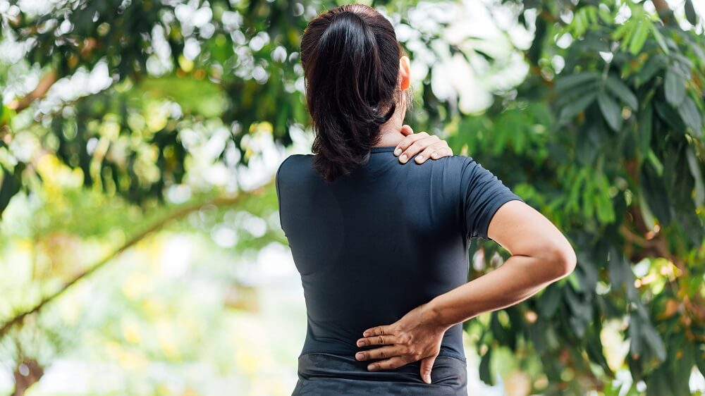 Frau mit Rückenschmerzen Schulter Nacken greift sich an Rücken und Nacken